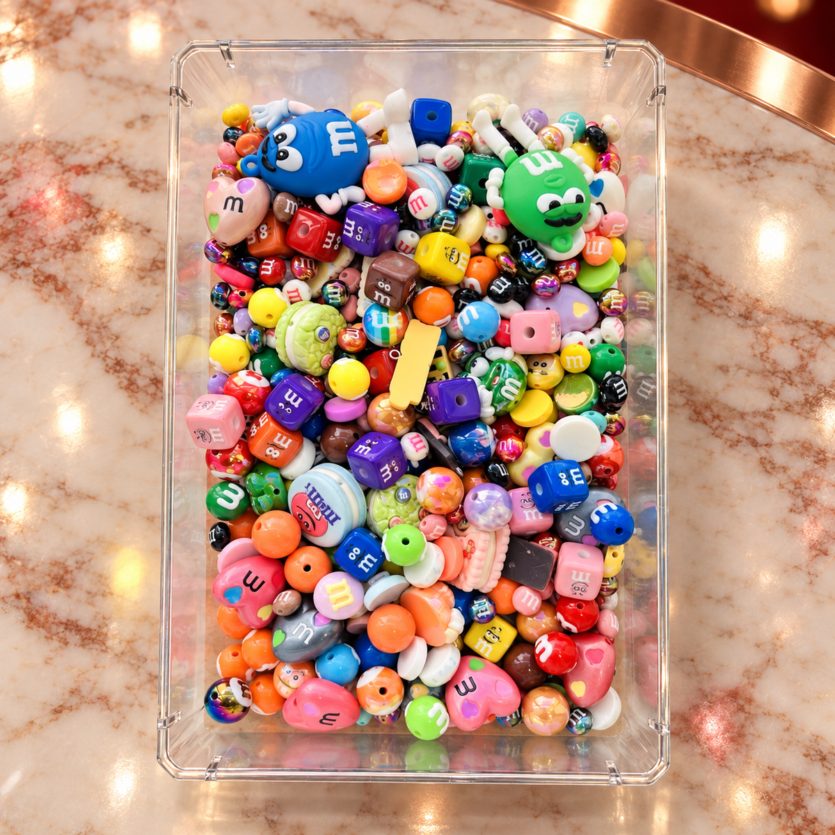 Overhead view of the Chocolate Candies bead mix in a clear rectangular tray, filled with colorful candy-inspired rounds, character cubes, hearts, cookie shapes, glossy accent beads and large blue and green character-inspired focal pieces.