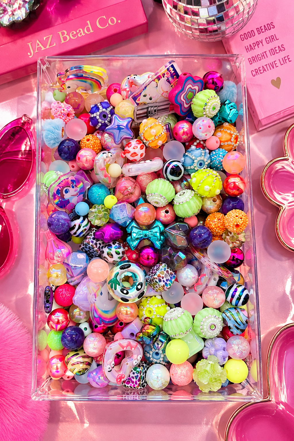 Overhead view of Cosmic Crush beads filling a clear rectangular tray, with bright pink, purple, aqua, lime, orange and pastel beads mixed with animal prints, stars, bows, geometric shapes, rhinestone details and whimsical focal pieces.