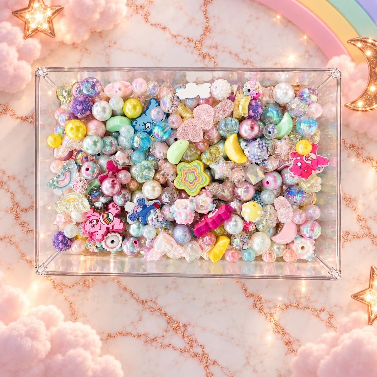 Overhead view of Care Buddies bead mix in a clear tray, featuring pastel pink, aqua, mint, lavender and yellow beads with pearl, iridescent and transparent finishes, stars, moons, flowers, rainbow details and playful character focal pieces.