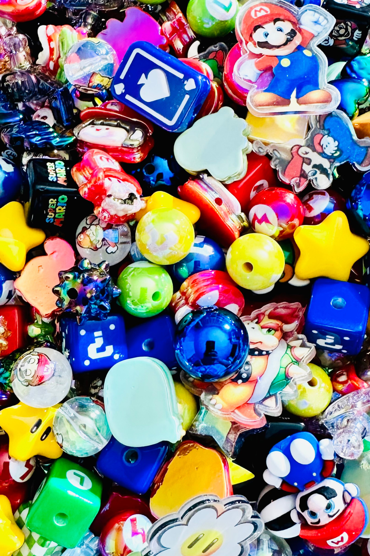 Close-up of the Retro Gamer bead mix showing blue question-mark cubes, green game-symbol blocks, character-inspired focal pieces, red hearts, glossy blue rounds, translucent beads, colorful game icons and dimensional arcade-inspired shapes.