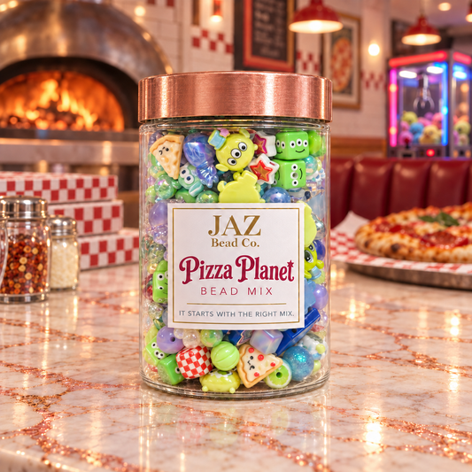 Pizza Planet bead mix spilling from a clear jar across a pizza-parlor counter, showing bright green character beads, three-eyed alien-inspired focals, red-and-white checkerboard cubes, blue and aqua rounds, stars, pizza pieces, bows and colorful dimensional accents.