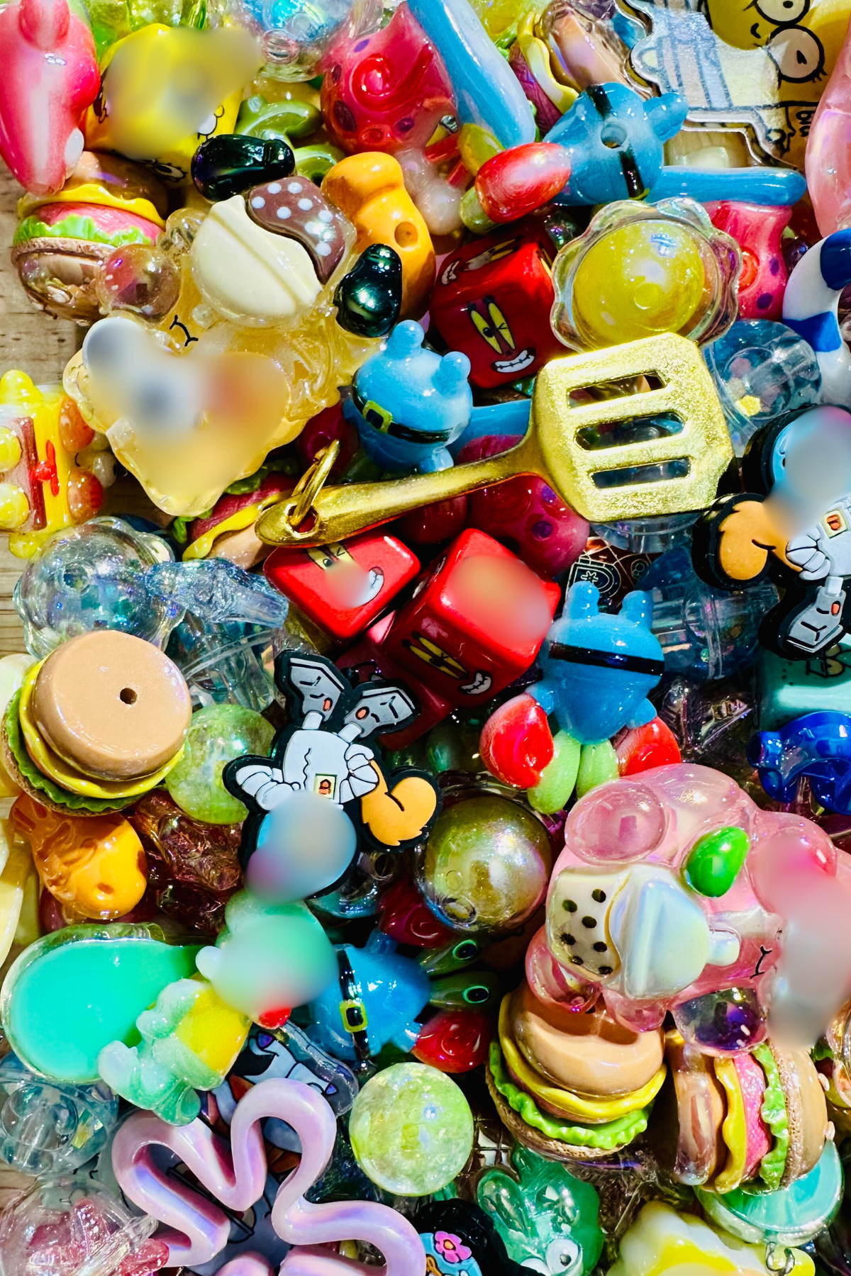 Close-up of the Krabby Patty bead mix showing colorful burger beads, character-inspired focal beads, pink and aqua cubes, sea-creature shapes, starfish, shells, glossy rounds, and clear and iridescent accents in pink, yellow, mint, aqua and blue.