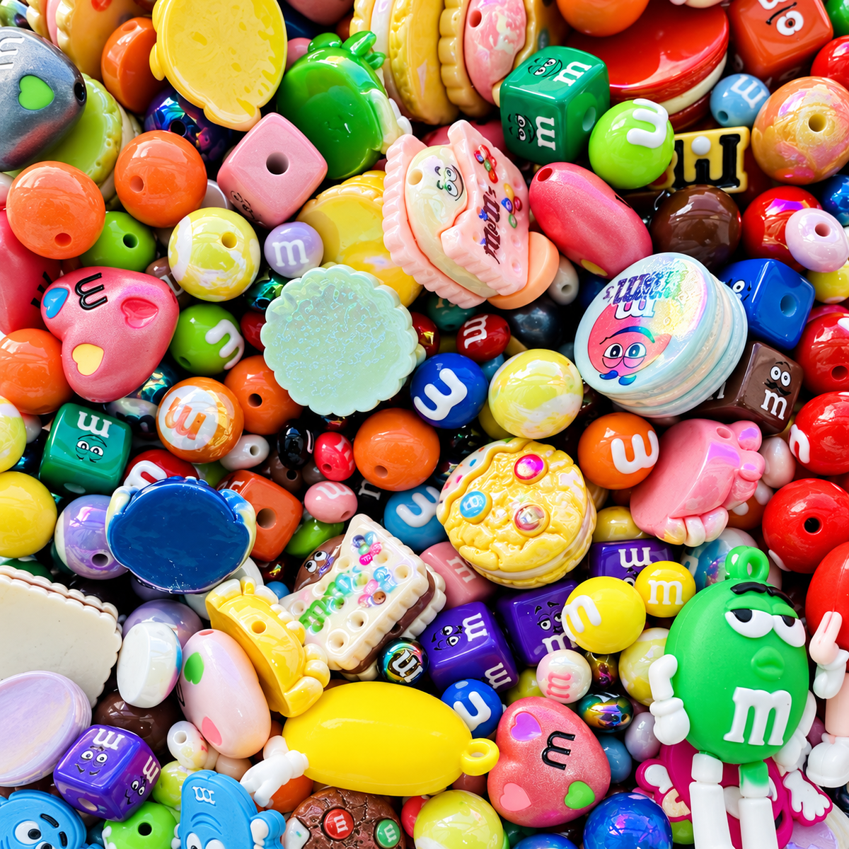 Chocolate Candies bead mix spilling from a clear jar across a marble candy-shop counter, showing colorful candy-inspired round beads, hearts, cubes, character focal pieces, cookie shapes and glossy multicolor accents.