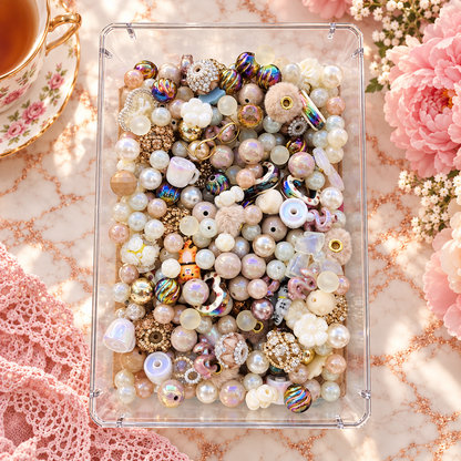 Overhead view of Memaw’s Pearls bead mix featuring creamy pearls, blush and neutral beads, iridescent accents, flowers, teacups, fuzzy beads and gold details in a clear tray.